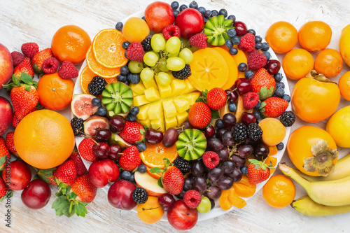 Healthy platter with colorful rainbow fruits  strawberries raspberries oranges plums apples kiwis grapes blueberries mango persimmon  top view  copy space