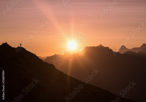 silhouette of a man standing on a mountain against a background of smoky mountains and bright dawn