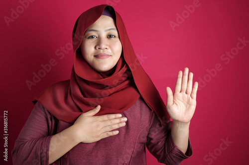 фотографія Asian muslim woman making pledge gesture, hand on chest, making promise