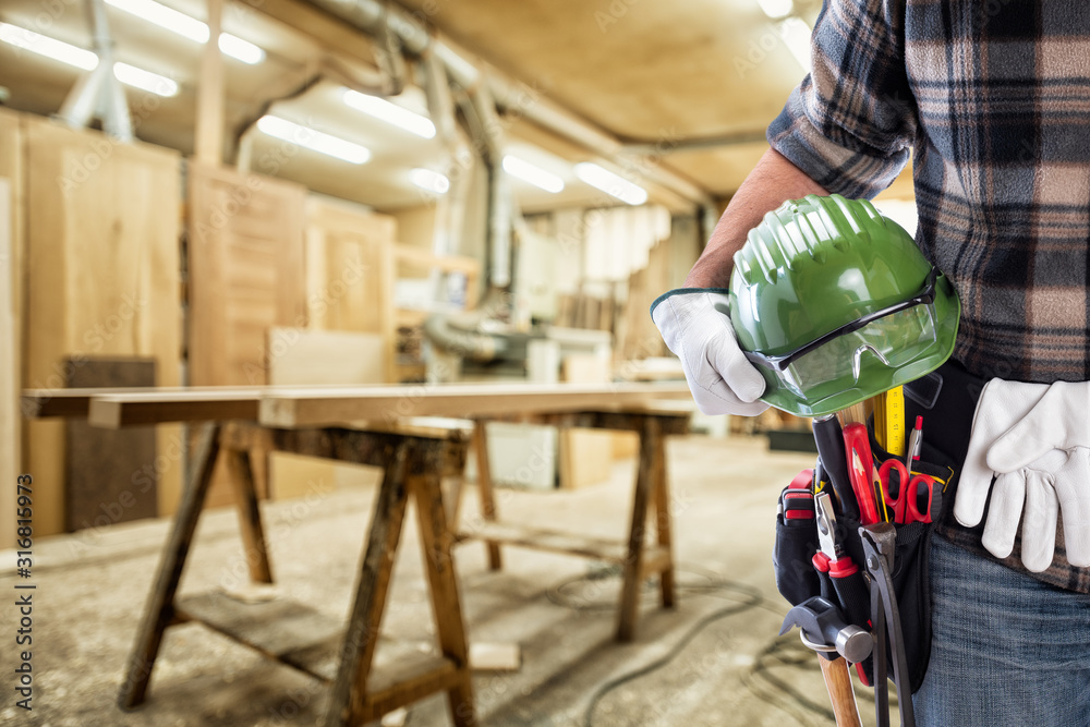 Close-up. Carpenter with hands protected by gloves holds helmet and protective goggles. Construction industry, carpentry workshop.