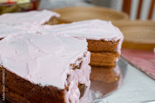 A girl pours a glaze of strawberry-flavored pink cream onto a two-tiered cake. homemade birthday cake,