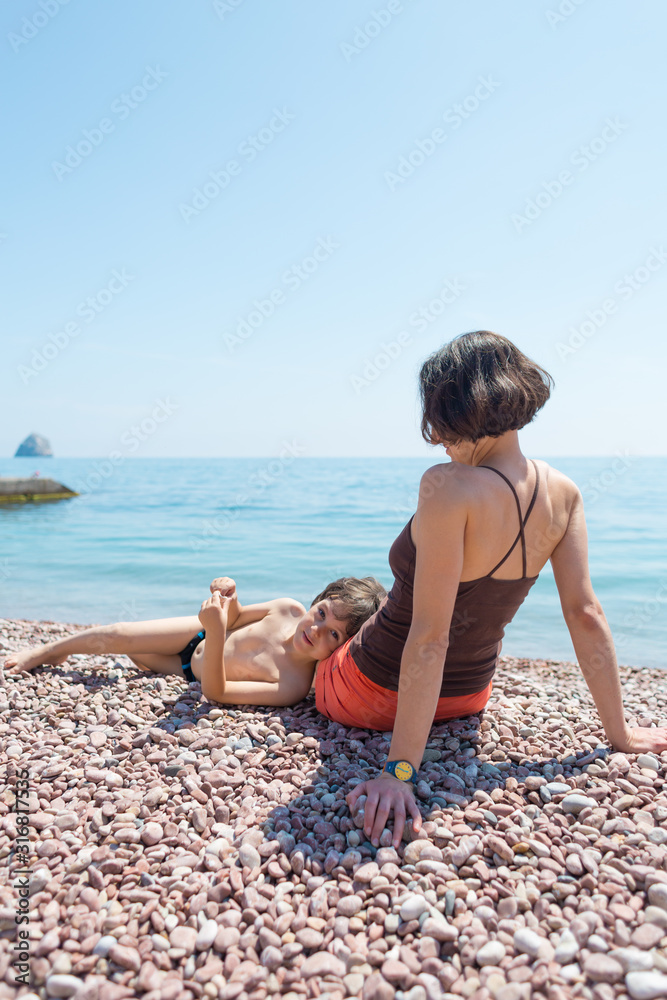 A woman sits with her son on the beach and looks at the sea. A woman sits with her son on the beach and looks at the sea.