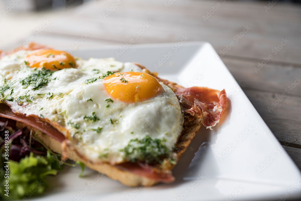 Meat sandwicht with fried eggs, salad on white plate and wooden table
