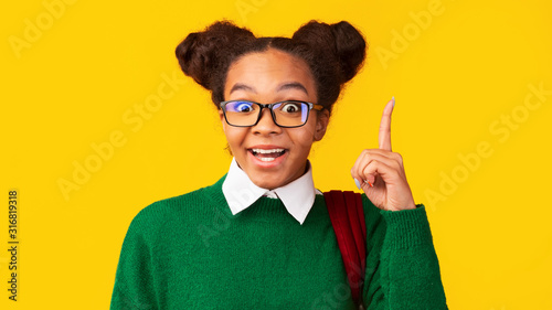 Afro teenager pointing up over yellow studio wall