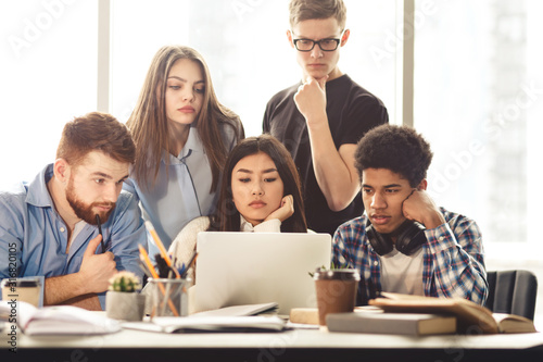 College classmates doing group project at library using laptop