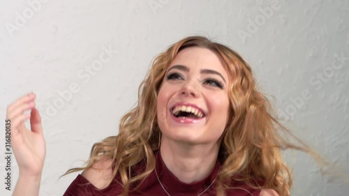 Young blonde girl lifts strands of hair up and throws them. Hair is flying in different directions. The face is hidden behind curls of hair. Clearly expressed emotions on the woman's face.