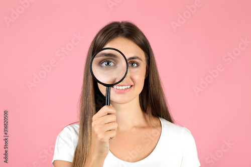 Young woman with magnifying glass on pink background