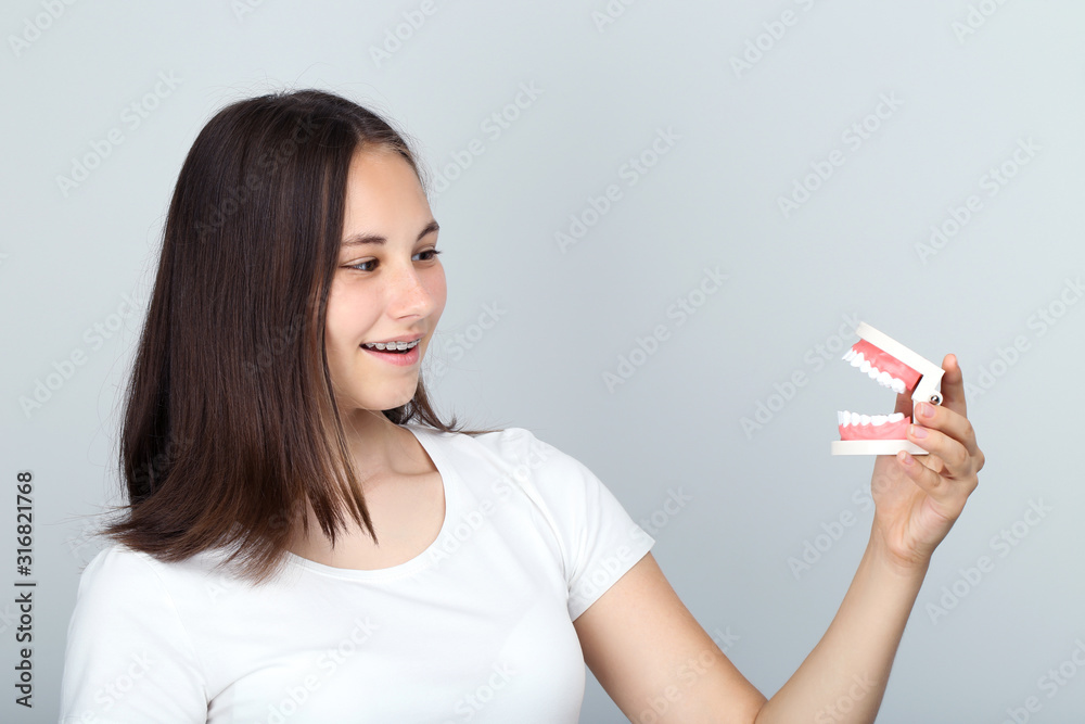 Young girl with dental braces holding teeth model on grey background Young girl with dental braces holding teeth model on grey background