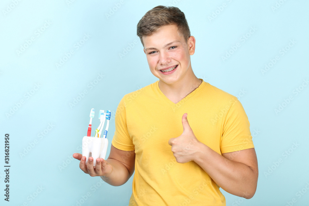 Young man with toothbrushes showing thumb up on blue background Young man with toothbrushes showing thumb up on blue background