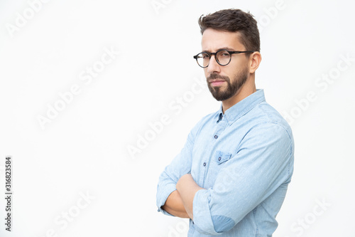 Confident young man looking at camera. Portrait of handsome serious young man standing with crossed arms and looking at camera on white background. Male beauty concept