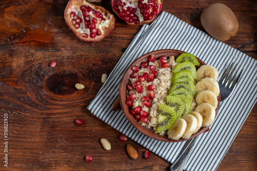 Breakfast consisting of oatmeal, nuts and fruits. Kiwi banana pomegranate almonds decorate a plate. Healthy food, on wooden background.
