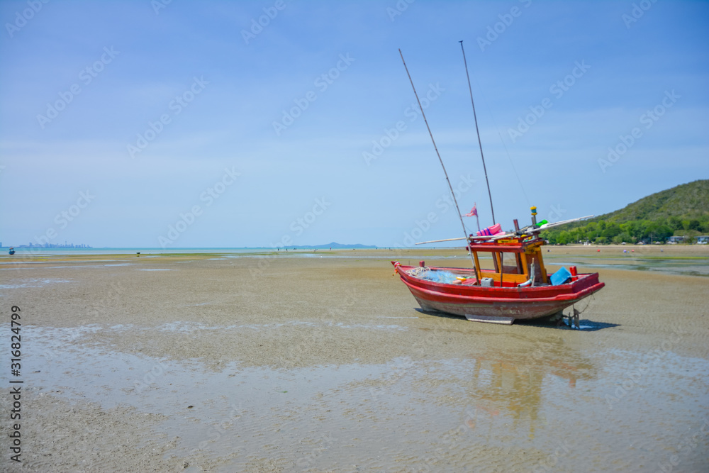 Fototapeta premium Fishing boat parked on the beach,Fishing boat parked on the seashore,Small fishing boat parked and moored on the beach at low tide. Boat and anchor at the beach in summer vacation. Sunny day.