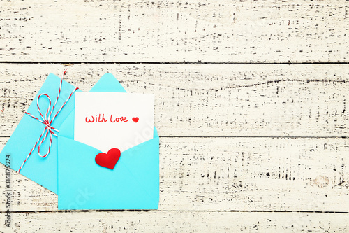 Blue paper envelopes with red heart and text With Love on white wooden table