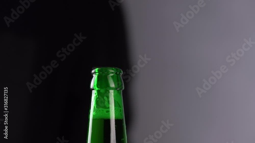 Man opening cold bottle of beer with cap on black background. Hands cracking refrigerated wheat or lager beer with an opener on dark background
