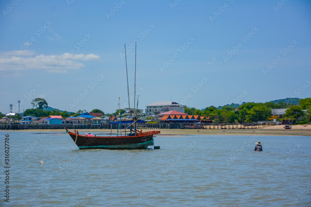 Fototapeta premium Fishing boat parked on the beach,Fishing boat parked on the seashore,Small fishing boat parked and moored on the beach at low tide. Boat and anchor at the beach in summer vacation. Sunny day.