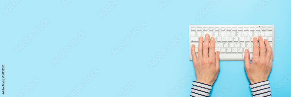 Female hands on a keyboard on a blue background. Concept of office work, freelance, online. Banner. Flat lay, top view Female hands on a keyboard on a blue background. Concept of office work, freelance, online. Banner. Flat lay, top view
