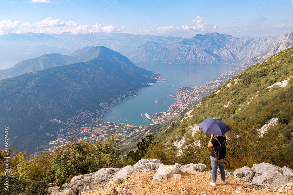 A tourist backpacker under black umbrella enjoying amazing view and taking photo of Kotor Bay, Montenegro. 