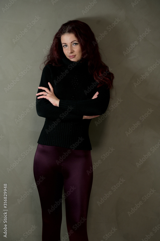 Portrait of a pretty slender brunette woman in a dark sweater and with brown hair stands on a gray background in the studio. The concept of fashionable art portrait of a glamorous model Portrait of a pretty slender brunette woman in a dark sweater and with brown hair stands on a gray background in the studio. The concept of fashionable art portrait of a glamorous model