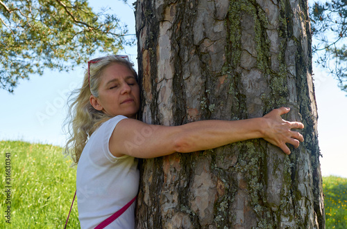 Woman hugging big old tree trunk in spring while showing emotions to endangered nature photo