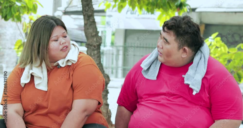 Young obese couple chatting together while sitting at the park after exercising. Shot in 4k resolution Young obese couple chatting together while sitting at the park after exercising. Shot in 4k resolution