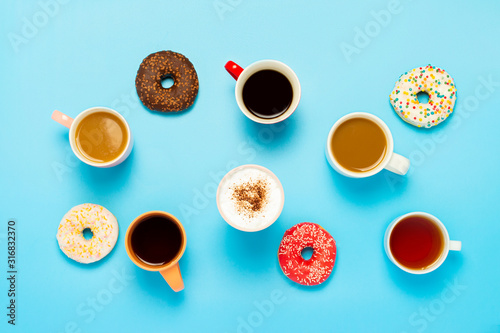 Tasty donuts and cups with hot drinks, coffee, cappuccino, tea on a blue background. Concept of sweets, bakery, pastries, coffee shop, meeting, friends, friendly team. Flat lay, top view