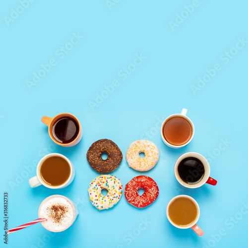 Tasty donuts and cups with hot drinks, coffee, cappuccino, tea on a blue background. Concept of sweets, bakery, pastries, coffee shop, meeting, friends, friendly team. The square. Flat lay, top view