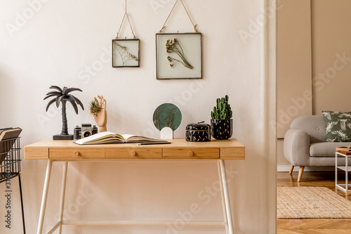 Interior design of scandinavian open space with mock up photo frames, wooden desk, gray sofa, cacti, books office and personal accessories. Stylish neutral home staging. Beige walls. Template.