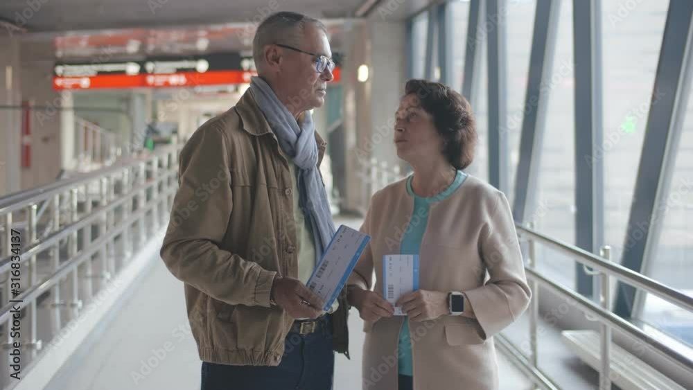 Happy mature travelers holding tickets and talking standing at railway station Happy mature travelers holding tickets and talking standing at railway station