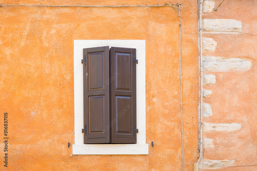 Fototapeta premium Old orange house facade, closed brown window shutters in popular touristic historic village Garda