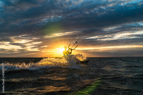 Silhouette of kitesurfer riding at the ocean in beautiful sunset condition with sun star and lens flare
