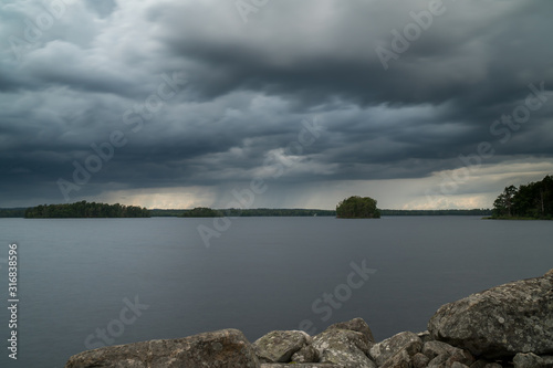 Landscape shot of thunderstorm with beautiful rainfall and dark clouds over a lake in sweden and rocks in the forground