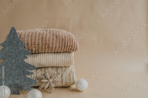 Background of beige colors with knitted sweaters, white balls, golden snowflakes and a felt gray Christmas tree. The concept of winter sales.