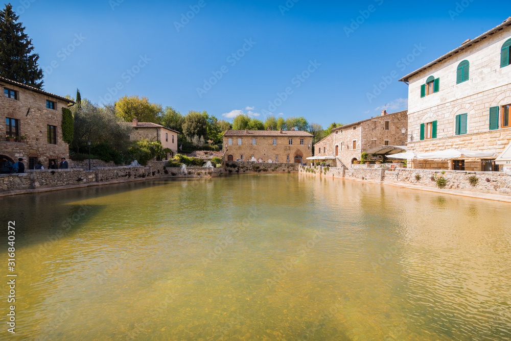 bagno vignoni natural thermal pool in a spring day with warm light sky with clouds in tuscany in italy typical small town historical village