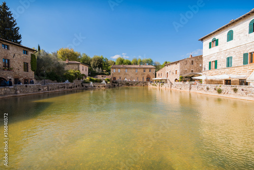 bagno vignoni natural thermal pool in a spring day with warm light sky with clouds in tuscany in italy typical small town historical village
