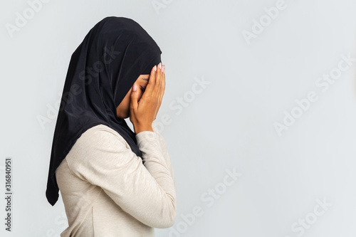 Profile portrait of desperate black muslim woman covering face with hands