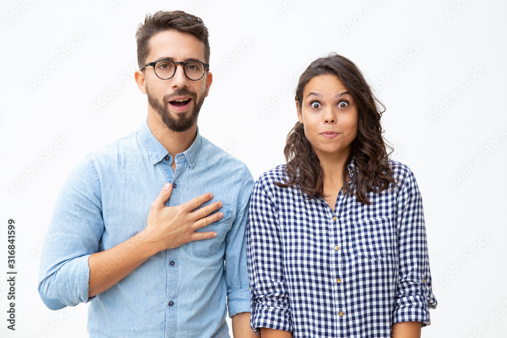 Shocked young couple looking at camera. Front view of scared young man and woman with wide open eyes standing together and looking at camera in white background. Emotion concept Shocked young couple looking at camera. Front view of scared young man and woman with wide open eyes standing together and looking at camera in white background. Emotion concept