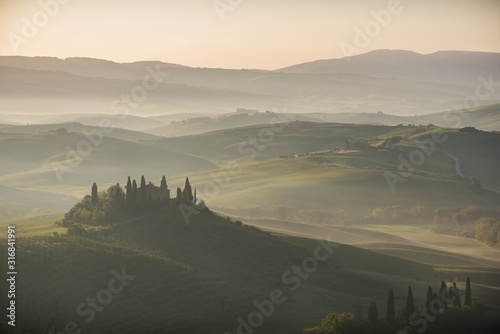Podere belvedere house on a hills in tuscany in italy at sunrise with beautiful light and myst and fog on sweet hills with cypresses trees