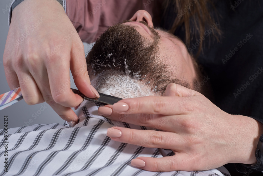 Close-up of the hand of a beard care professional. cutting a beard for a young man with a dangerous razor
