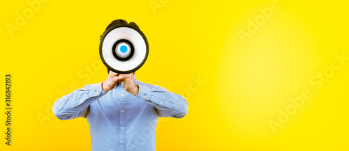man with a megaphone over yellow background, panoramic image with space for text, announcement concept photo