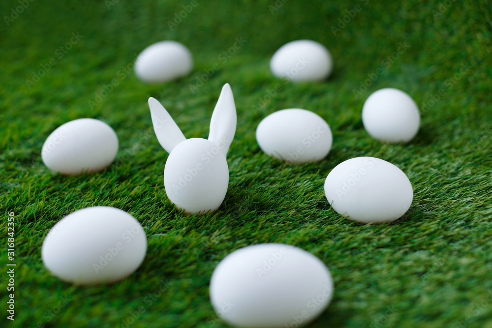 White chicken eggs on green grass, behind which are hidden the ears of the Easter bunny, which are symbols for the celebration of religious holiday among Christians and Catholics. White chicken eggs on green grass, behind which are hidden the ears of the Easter bunny, which are symbols for the celebration of religious holiday among Christians and Catholics.