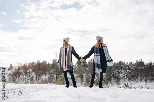 Cute girls walking in a winter park. Sisters have fun with snow. Ladies in a cute hats