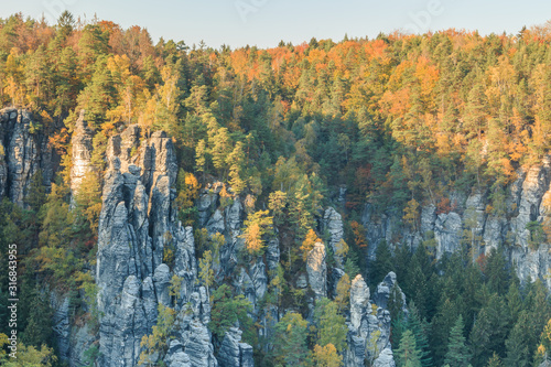 Rock formation in Saxon Switzerland. Elbe Sandstone Mountains in autumn mood with rocks and trees under blue sky and sunshine. Valley near the Bastei bridge