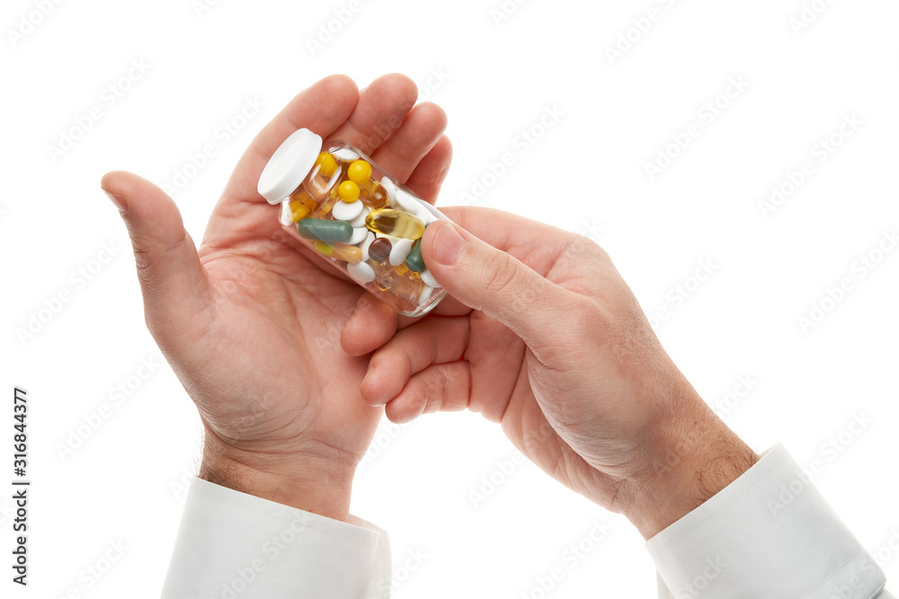 Man hand with glass bottle full of pills, tablets, vitamins, drugs, capsules isolated on white background. White shirt, business style. Health care concept. Pharmaceutical industry. Pharmacy. Man hand with glass bottle full of pills, tablets, vitamins, drugs, capsules isolated on white background. White shirt, business style. Health care concept. Pharmaceutical industry. Pharmacy.