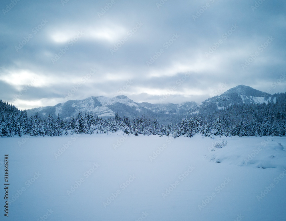 Snow covered frozen beautiful Gold Creek Pond with snow covered trees and trail during the winter in the Alpine Lakes Wilderness in Kittitas county Washington State