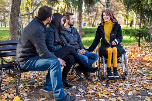 Disabled young woman in a wheelchair enjoying with friends in the park