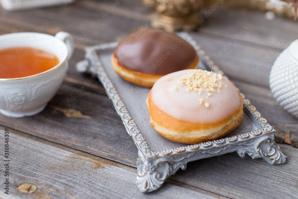 Donuts made of white milk chocolate, coated with glaze and nuts. Aristocratic tea party with porcelain cup on wooden table. Decorated with vases,cotton inflorescences,white sugar bowl.Gold background Donuts made of white milk chocolate, coated with glaze and nuts. Aristocratic tea party with porcelain cup on wooden table. Decorated with vases,cotton inflorescences,white sugar bowl.Gold background