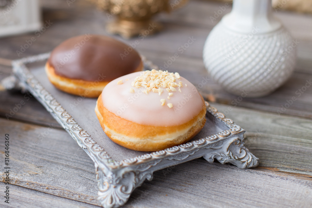 Donuts made of white milk chocolate, coated with glaze and nuts. Aristocratic tea party with porcelain cup on wooden table. Decorated with vases,cotton inflorescences,white sugar bowl.Gold background Donuts made of white milk chocolate, coated with glaze and nuts. Aristocratic tea party with porcelain cup on wooden table. Decorated with vases,cotton inflorescences,white sugar bowl.Gold background