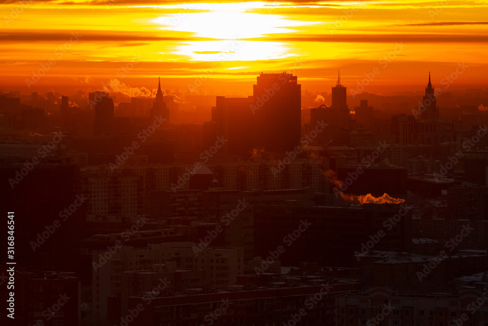 Fototapeta premium Sunrise over the city. Aerial view of Moscow, silhouettes of buildings in downtown with colorful lighting sunrise sky and soft clouds. Factories pipe, of which there are smoke. Rising sun