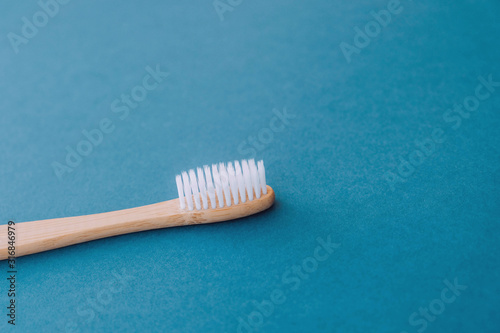 Stylish natural eco friendly toothbrush with wooden bamboo handle on blue background.