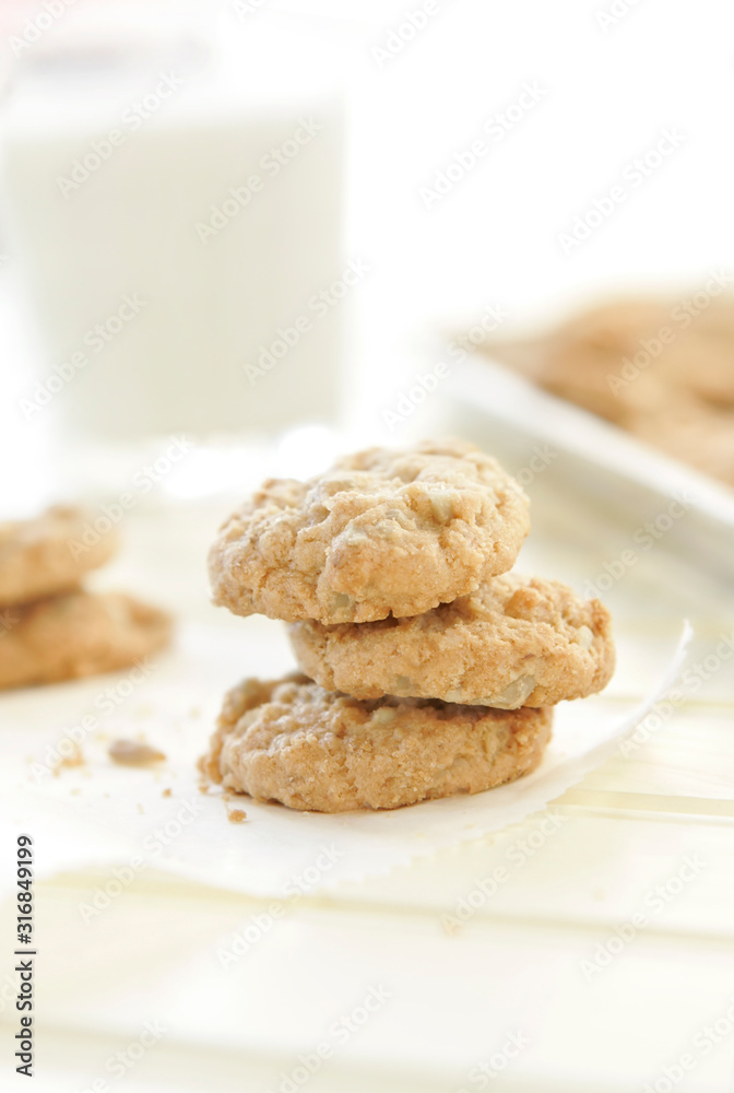 Stack of three sunflower seed cookies sitting on white parchment paper with a glass of milk and pan of cookies in the background Stack of three sunflower seed cookies sitting on white parchment paper with a glass of milk and pan of cookies in the background